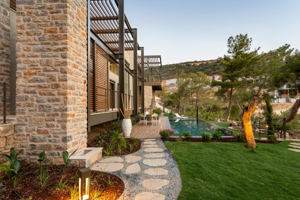 Modern villa in Bodrum featuring a stone facade, lush garden, and infinity pool with scenic views.